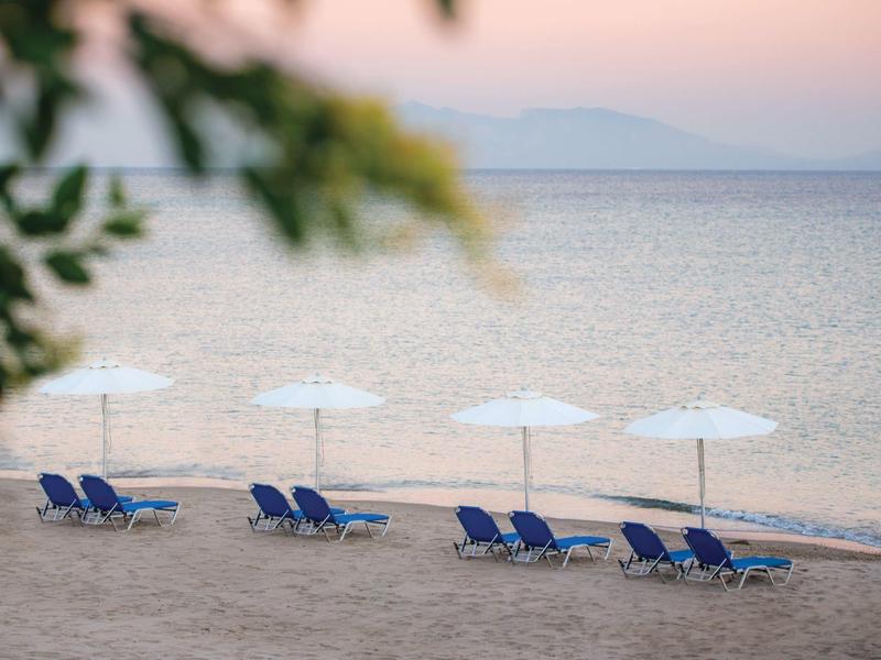 Lettini vuoti sotto ombrelloni bianchi su una spiaggia di sabbia tranquilla all'alba.