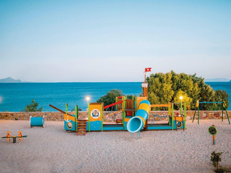 Parco giochi colorato con scivoli e strutture per arrampicata vicino alla spiaggia sotto un cielo azzurro.
