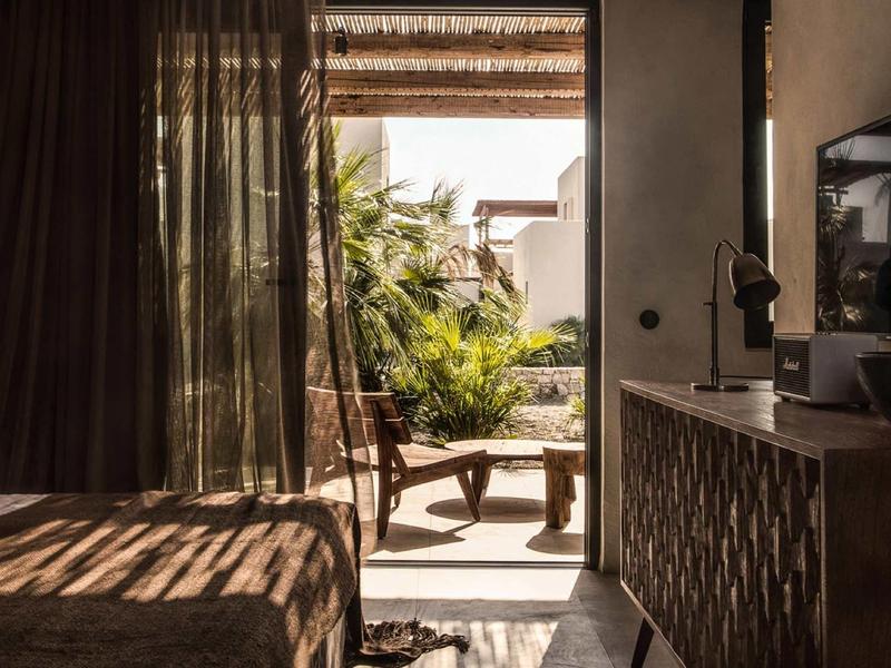 Gemütliches Zimmer mit Holzstuhl, Tisch und Pflanzen, Licht durch Gardinen fällt ins Zimmer.