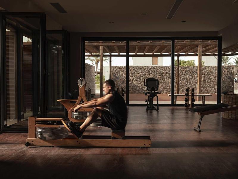 Frau trainiert auf Rudergerät in einem dunklen, geräumigen Fitnessraum mit großen Fenstern.