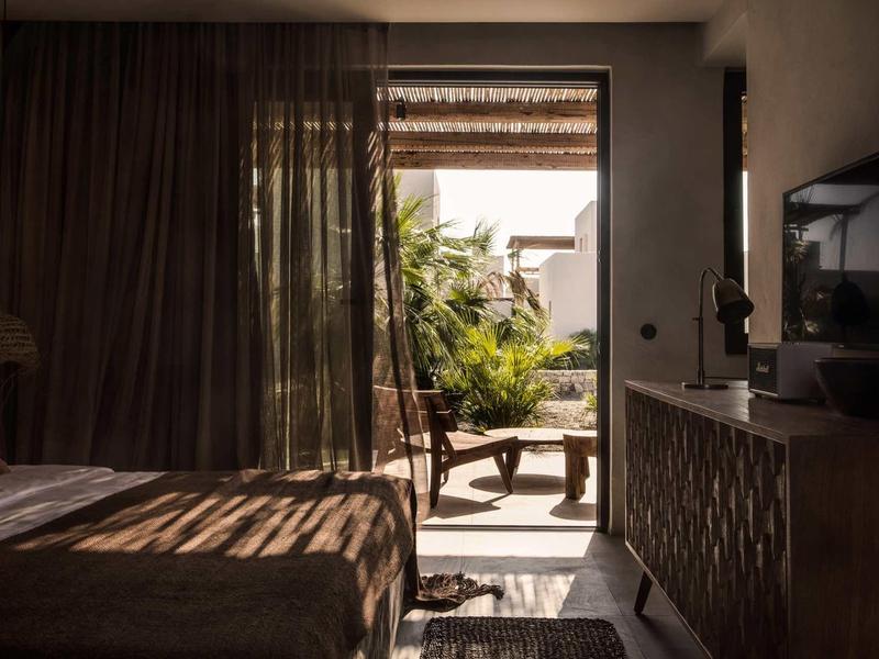 Schlafzimmer mit geöffnetem Tür zu Terrasse, dunkelbraune Möbel, Tageslicht, Pflanzen draußen.