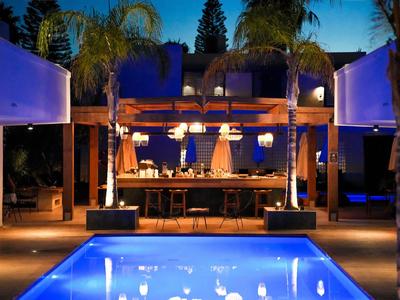 Moderner Außenbereich mit beleuchtetem Pool und Bar unter Palmen bei Nacht.
