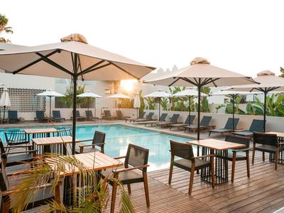 Moderner Hotelpoolbereich mit Holzterrasse, Sonnenliegen und großen Sonnenschirmen bei Sonnenuntergang.