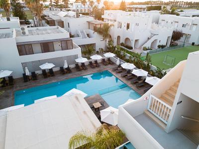 Moderner Hotelkomplex mit Pool, Liegestühlen und Sonnenschirmen bei Sonnenuntergang.
