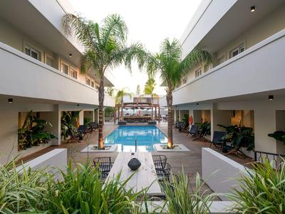 Moderner Hotelinnenhof mit Pool, Palmen und Sitzbereichen in warmem Licht.
