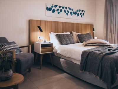 Modernes Hotelzimmer mit großem Bett, Holzkopfteil, Nachttisch und Sitzbereich in neutralen Tönen.