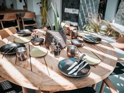 Runder Holztisch im Sonnenlicht mit gedecktem Frühstück für mehrere Gäste im Hotel.