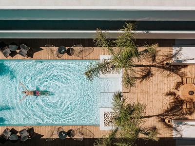 Vogelperspektive eines Hotels mit Pool und Sitzbereich unter Palmen.