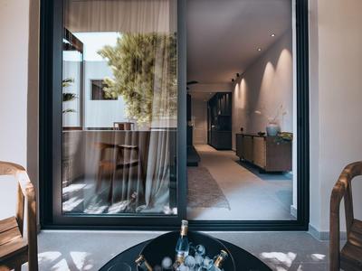Blick durch eine Glasschiebetür auf ein modernes Hotelzimmer mit Balkon und Sitzgelegenheiten.