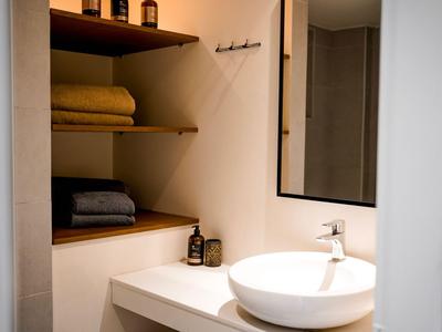 Modernes Badezimmer mit rundem Waschbecken, Spiegel und offenen Regalen mit Handtüchern.