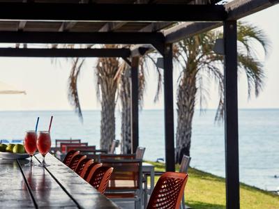 Bar all'aperto con bevande e vista sul mare, circondata da palme e sedie.