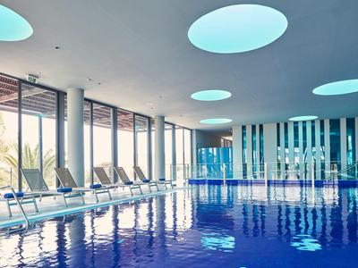 Piscina interna luminosa con lettini e grandi finestre.