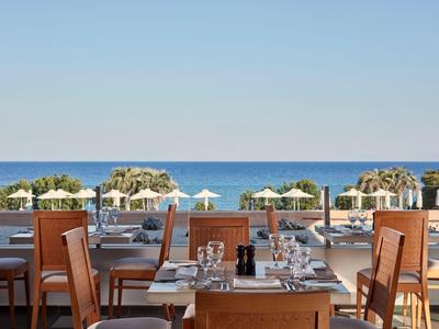 Ristorante con tavoli e sedie in legno con vista sul mare e ombrelloni