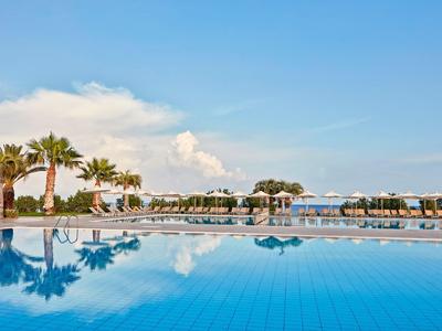 Grande piscina dell'hotel con palme e lettini sotto un cielo azzurro limpido.