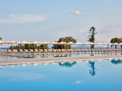 Piscina con ombrelloni e lettini, vista sul mare sotto un cielo limpido