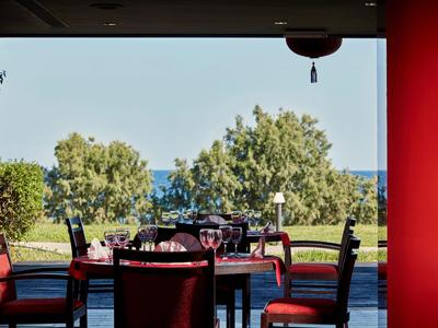 Zona pranzo con sedie rosse imbottite con vista su giardino e mare.