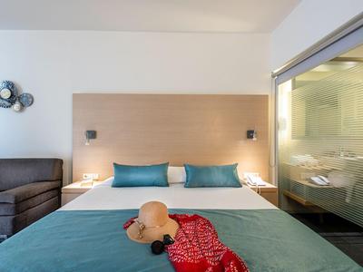 Camera d'hotel moderna con letto matrimoniale, comodini, divano e vista sul bagno.