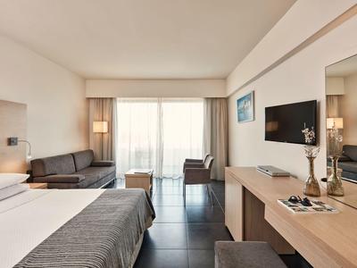 Camera d'hotel moderna con letto, divano, scrivania e grande finestra con tende.