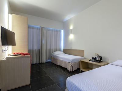 Camera d'hotel moderna con due letti singoli, TV a schermo piatto e finestra con tende.