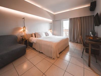 Modern eingerichtetes Hotelzimmer mit Doppelbett, Sofa, Schreibtisch und Balkon.
