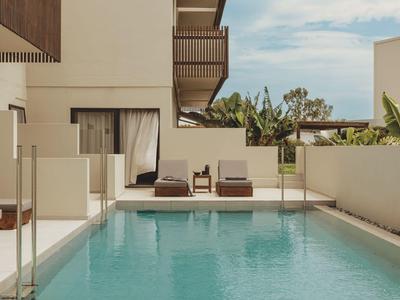 Moderner Hotelpool mit Liegestühlen und Blick auf tropische Pflanzen bei klarem Himmel.