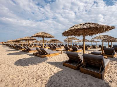 Mehrere Sonnenliegen mit Strohdächern auf einem sandigen Strand unter bewölktem Himmel.
