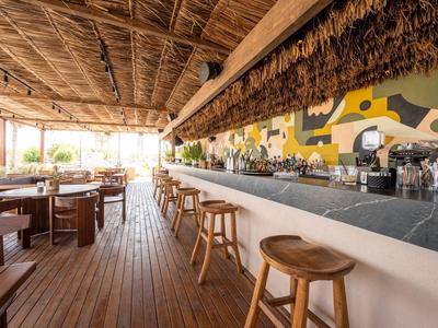 Offene Bar mit Holztheke und Hockern unter einem Dach aus Palmenblättern in einem tropischen Hotel.