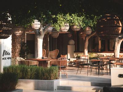 Gemütliche Außenbestuhlung eines Restaurants mit warmem Licht und viel Grün in der Abenddämmerung.