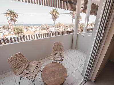 Balkon mit zwei Stühlen und einem kleinen Tisch mit Blick auf Palmen und das Meer.
