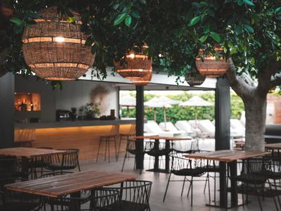 Gemütlicher Außenbereich einer Hotelbar mit hängenden Laternen und Holzmöbeln unter Bäumen.