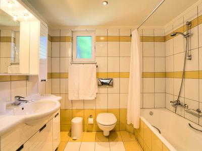 Helles Badezimmer mit Badewanne, Toilette, Waschbecken und Handtuchhalter unter Fenster.