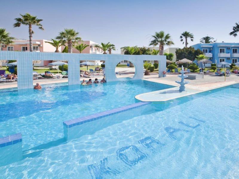 Großer Pool mit Brücke und Sonnenschirmen in einem Hotel mit blauen und weißen Gebäuden.