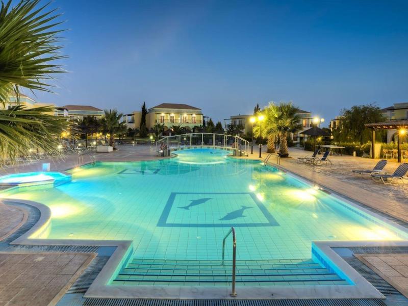 Großer beleuchteter Poolbereich mit Liegestühlen und Palmen bei Abenddämmerung.