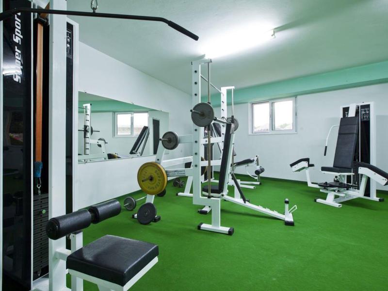 Ein Fitnessraum mit verschiedenen Trainingsgeräten und grünem Kunstrasenboden.