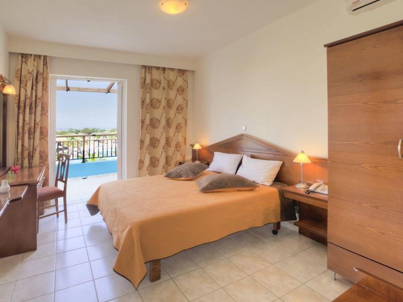Helles Hotelzimmer mit Doppelbett, Balkon mit Blick auf Wasser und Terrasse.