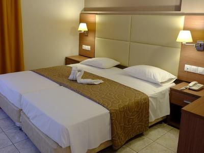 Hotelzimmer mit Doppelbett, braunen Vorhängen, zwei Nachttischen und weicher Beleuchtung.