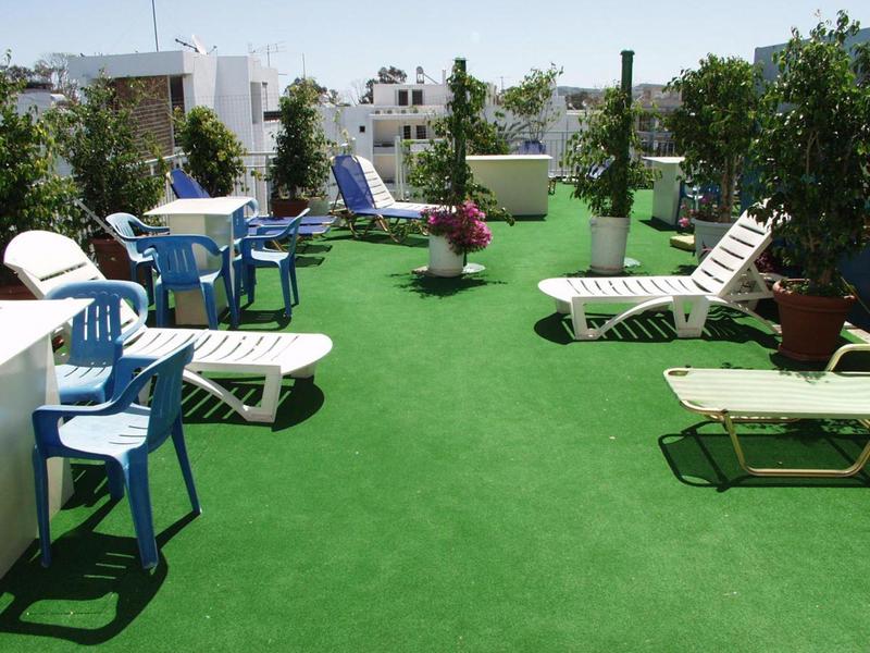 Grüne Dachterrasse mit weißen und blauen Stühlen, Liegestühlen und Pflanzkübeln im Freien.