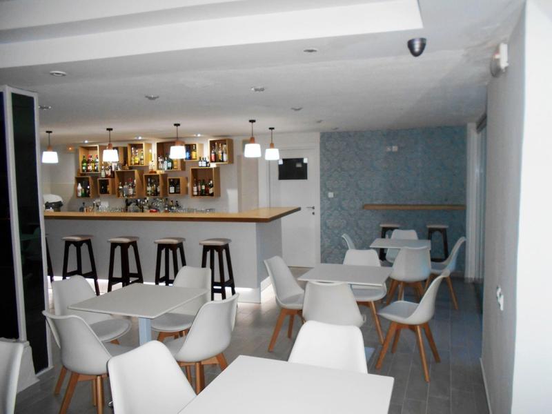 Moderne Bar mit weißen Stühlen, Holztischen, Barhockern und hellen Deckenleuchten in hellem Raum.