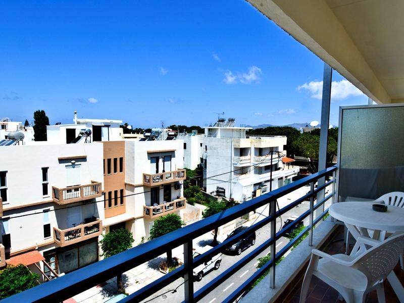 Balkon mit weißen Stühlen und Tisch, Blick auf weiße Wohngebäude unter blauem Himmel.