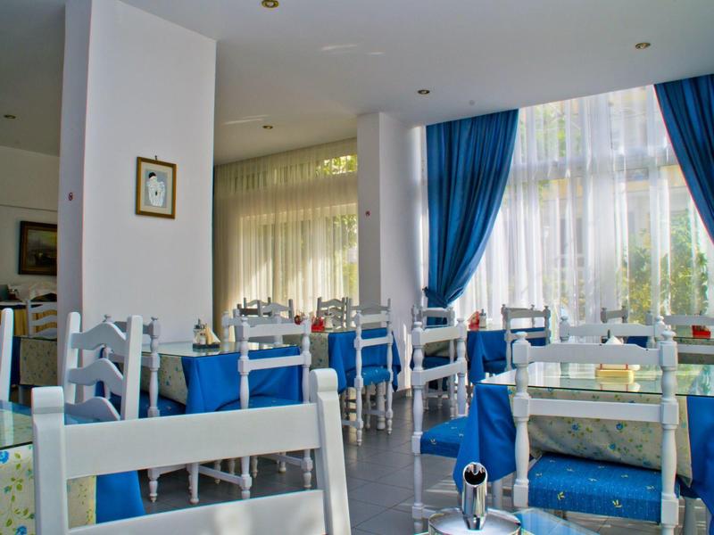 Helles Restaurant mit weißen Stühlen, blauen Vorhängen und großen Fenstern, lichtdurchflutet.