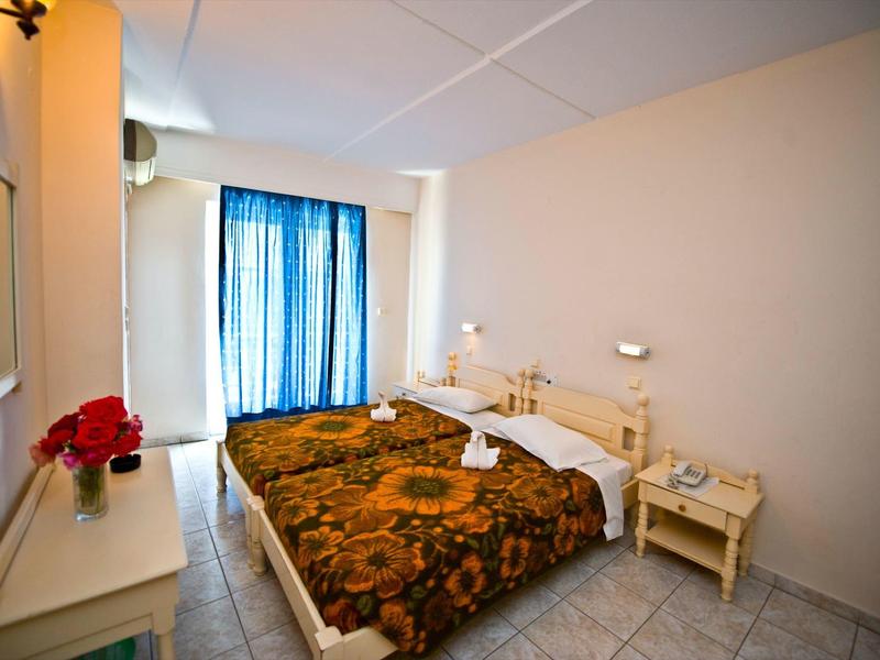 Hell eingerichtetes Schlafzimmer mit Doppelbett, blauen Vorhängen und kleinem Nachttisch.