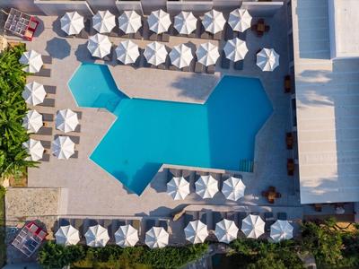 Vista aerea di una piscina blu circondata da ombrelloni bianchi e lettini accanto a un edificio.
