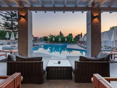 Vista da una terrazza coperta su una piscina con lettini al tramonto.