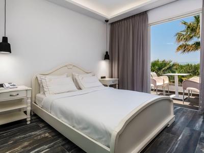 Bright hotel room with white bed, nightstands, and view of tropical plants