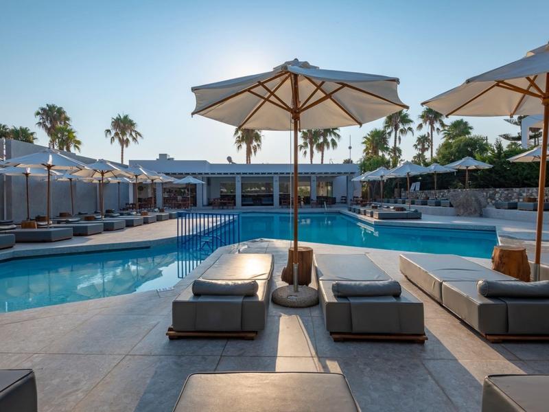 Modern hotel pool area with loungers and umbrellas at sunset.