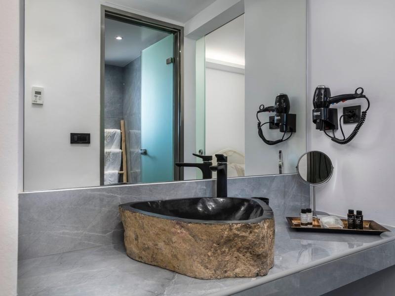 Modern hotel bathroom sink with stone basin and wall-mounted hairdryer.