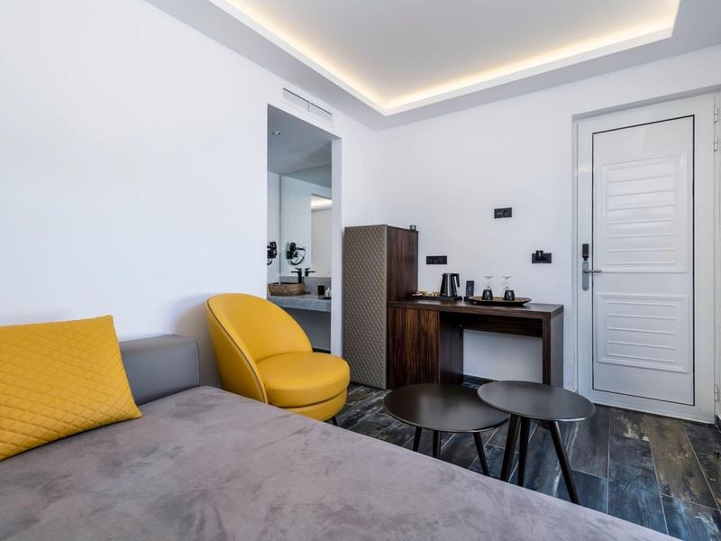 Modern hotel room with sofa, yellow armchair, desk, and decorative lighting.