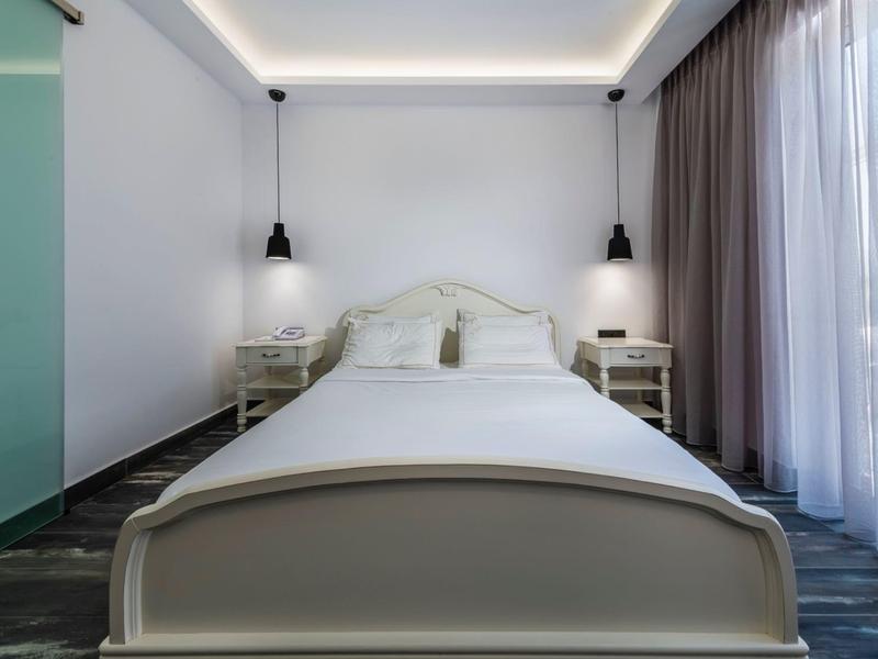 Simple single room with a bright bed, two nightstands, and large windows with curtains.