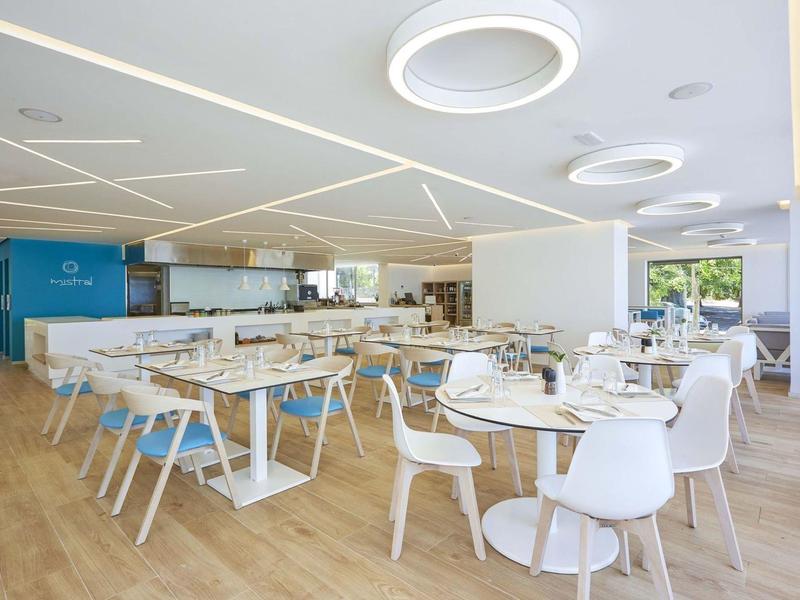 Modern, licht restaurant met witte tafels, blauw-witte stoelen en natuurlijke houten vloeren.