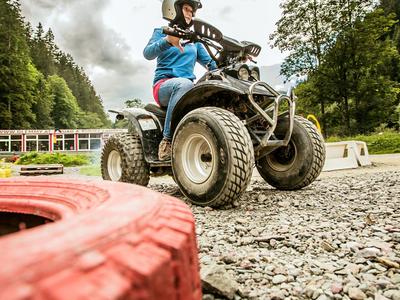 Person fährt ATV auf Schotterweg mit rotem Reifen im Vordergrund in naturreicher Umgebung